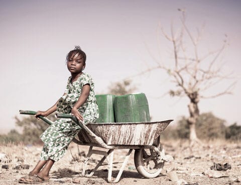 Foto av jente med trillebåre og vannkanne i tørt land.